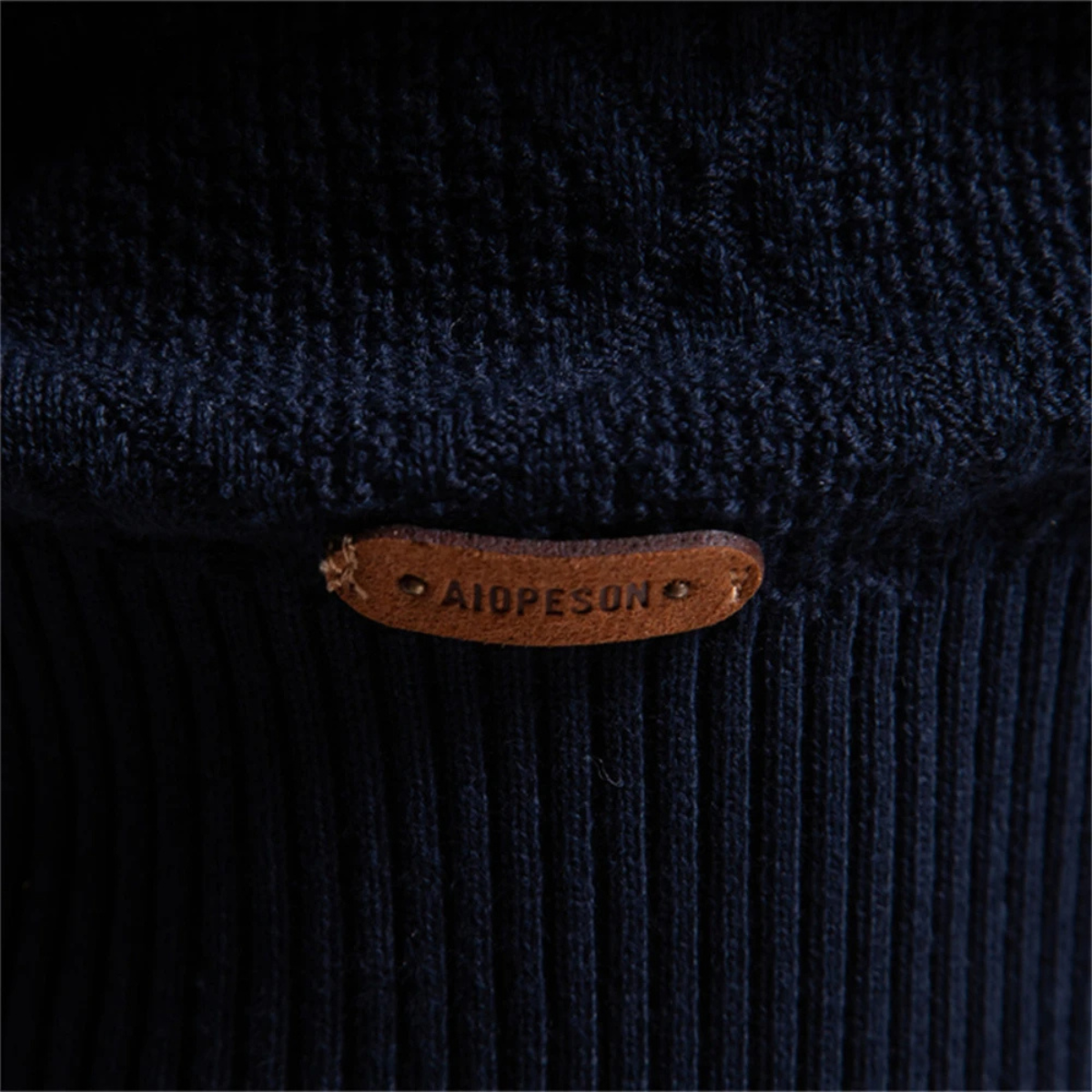 Men's polo sweater hem close-up with leather brand patch on dark knit