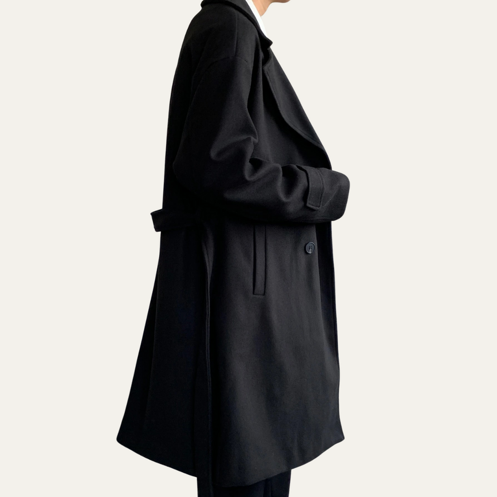 Black wool overcoat side view with waist tie detail and long length
