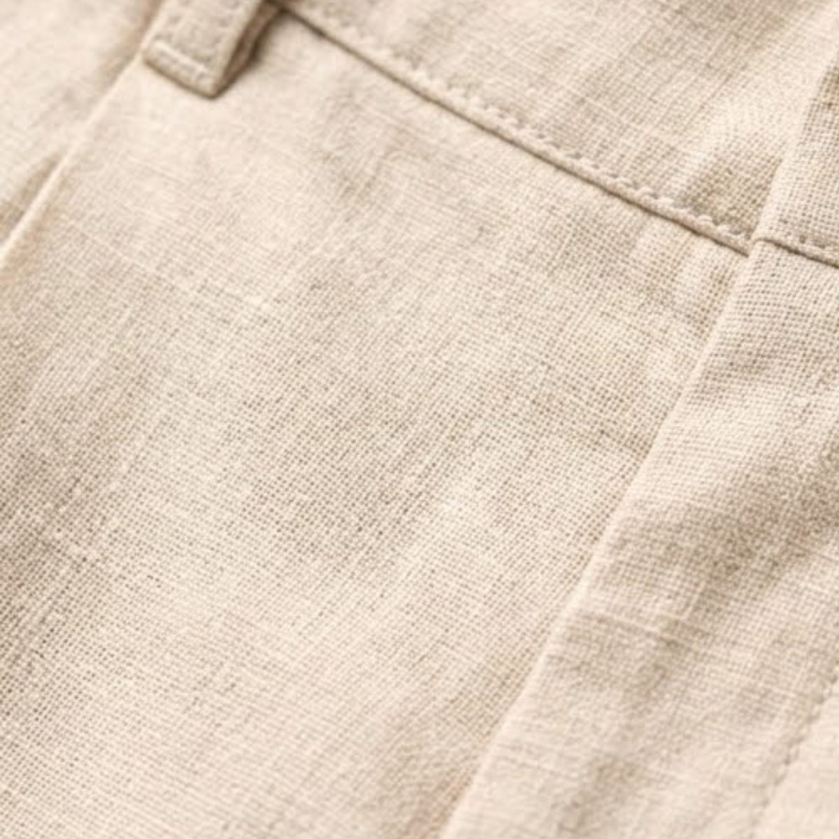 Light beige linen dress pants fabric close-up with stitched seam and waistband edge.