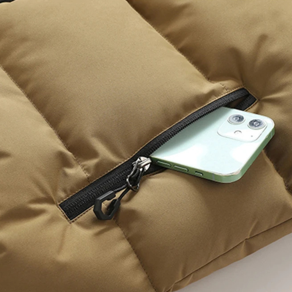Khaki padded vest with black zipper and zippered pocket holding a smartphone