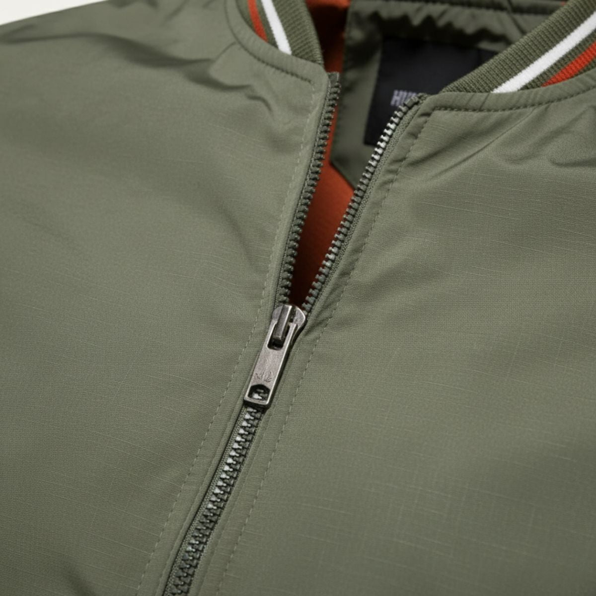 Sage green bomber jacket close-up: metal zipper and stitched placket