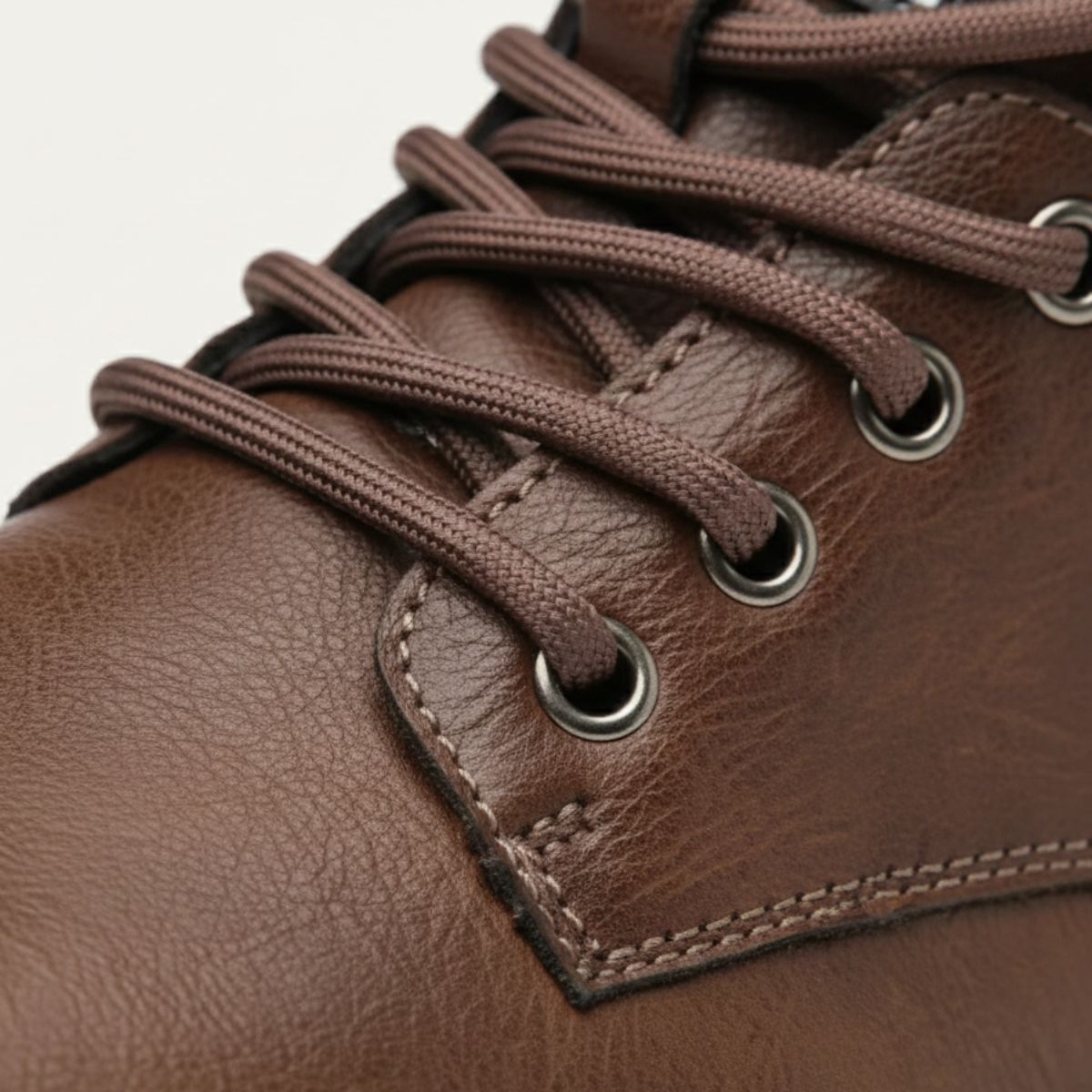 Brown leather boot laces close-up with metal eyelets and stitched panel detail