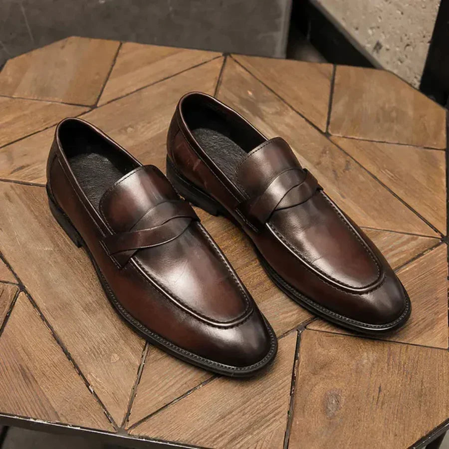 Brown leather penny loafers pair on wooden surface, slip-on moc stitching