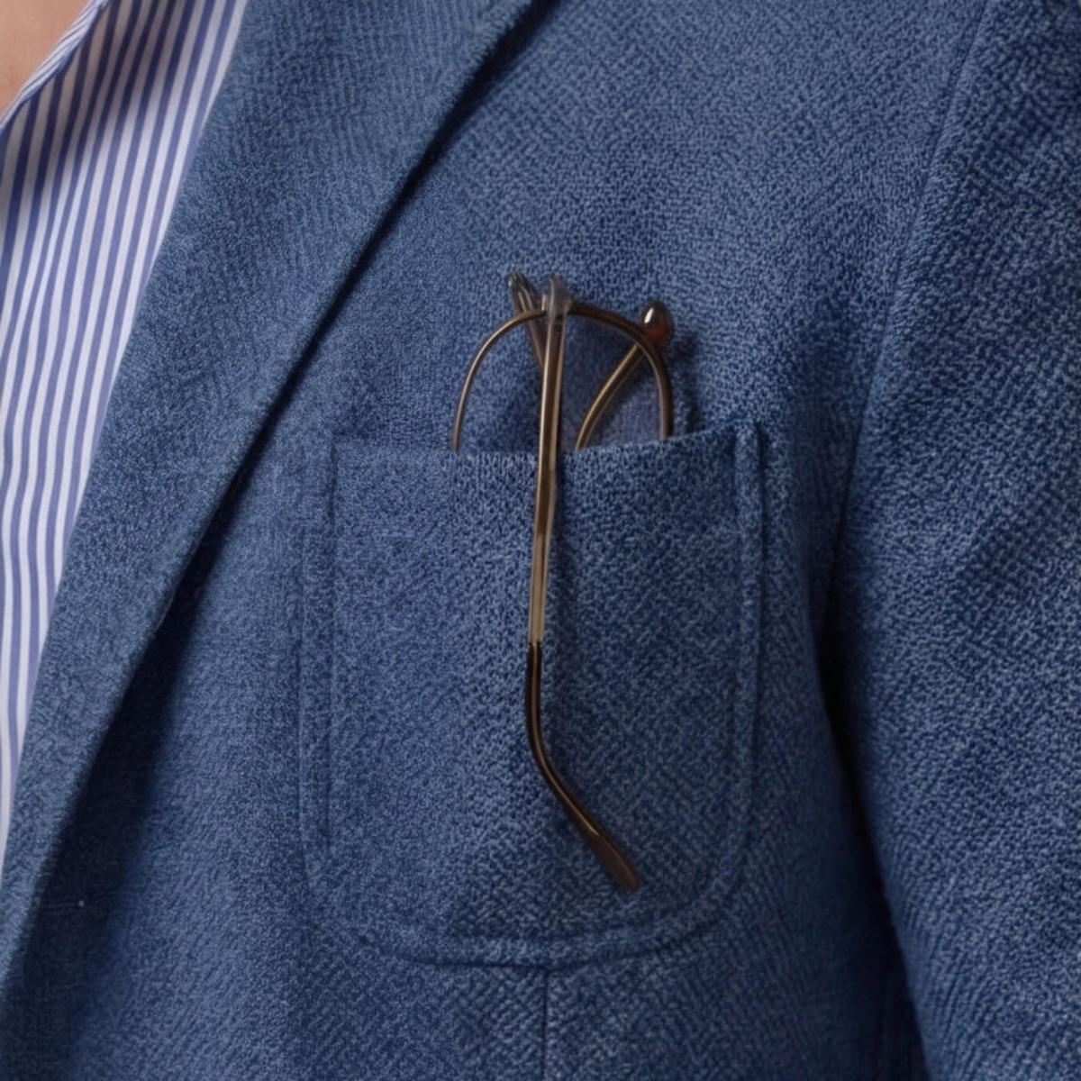 Men's blazer in blue, close-up of chest pocket with brown accessory and pocket stitch detail.