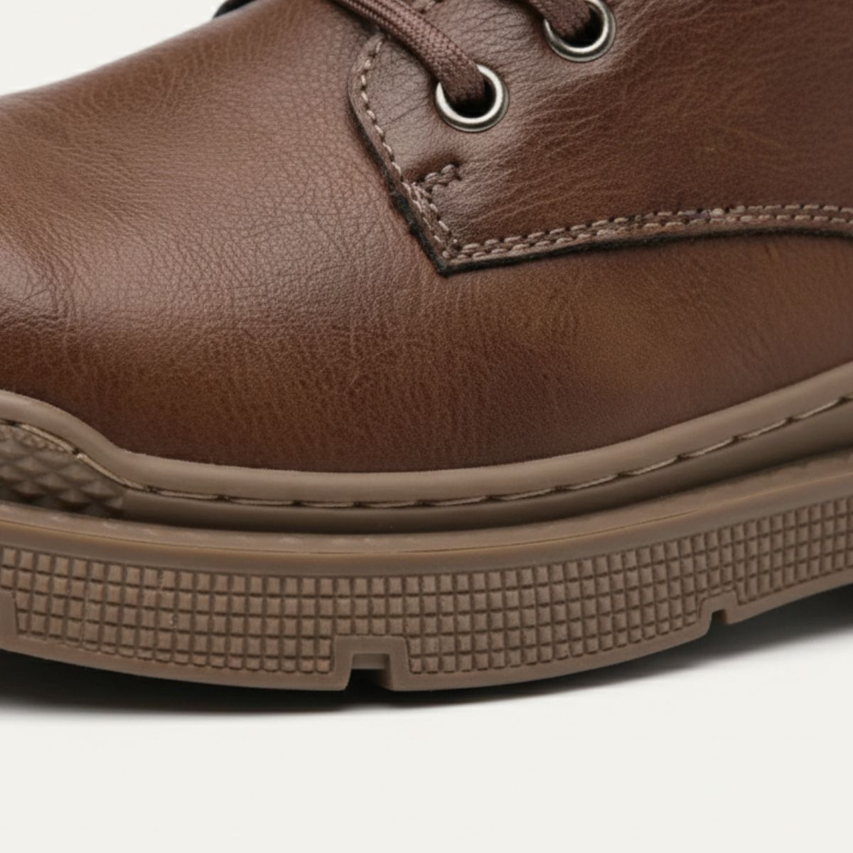Brown leather boot toe and side, showing eyelets, stitching, and cushioned sole