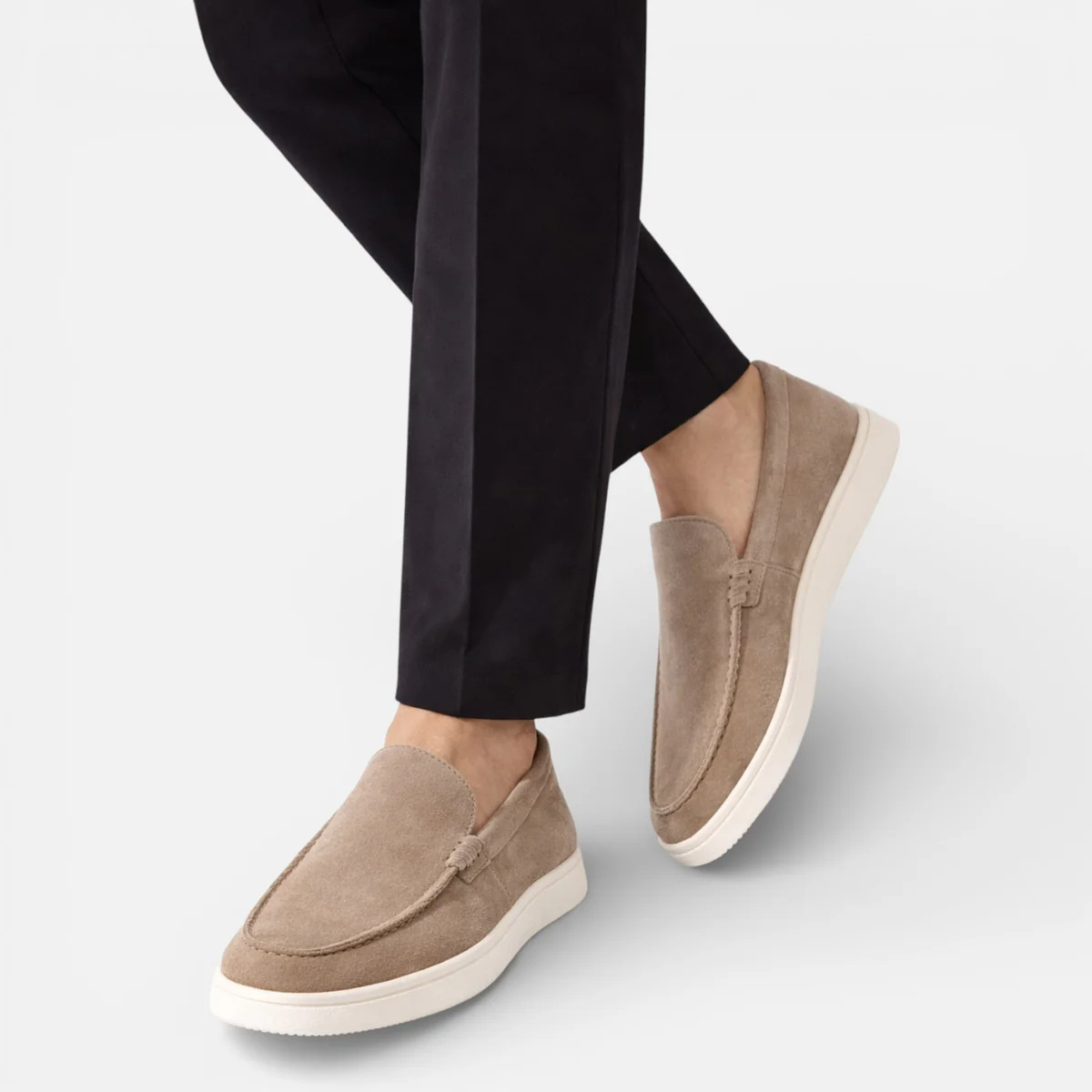 Beige suede slip-on loafers on feet with moccasin stitching and low white sole