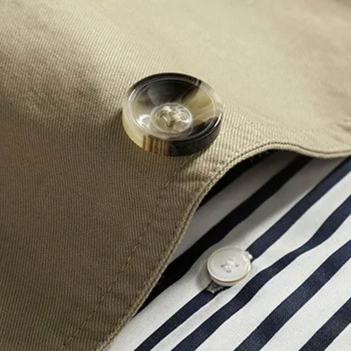 Men's tan trench coat lapel with button detail over striped inner fabric