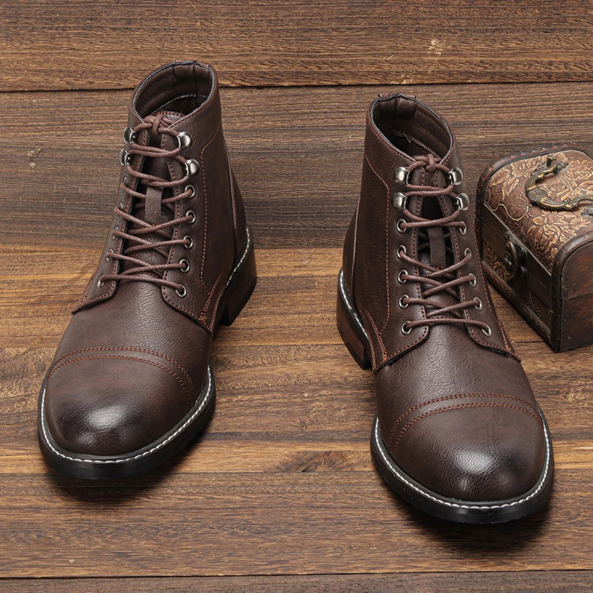 Men's brown lace-up ankle boots on wooden surface with metal eyelets and stitched toe cap
