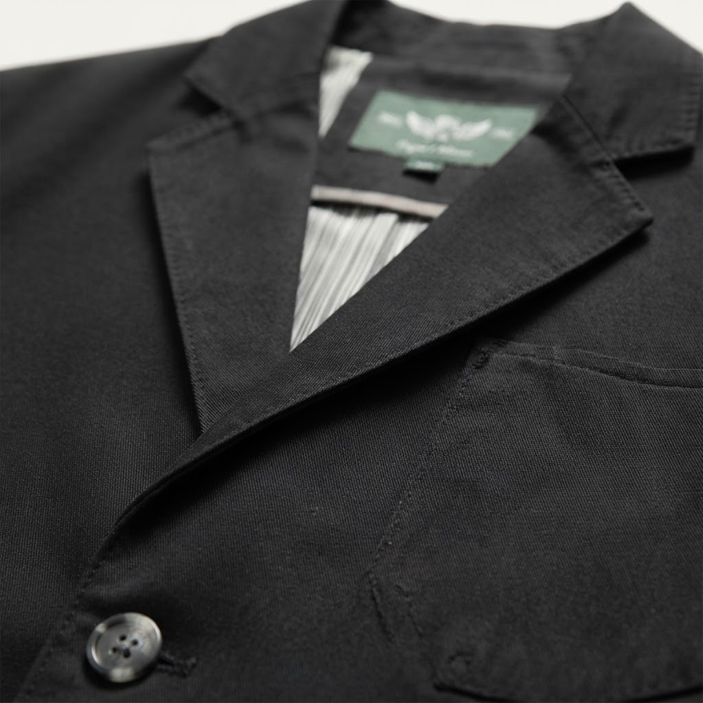 Close-up of dark blazer lapel with button detail and inner label at the neckline