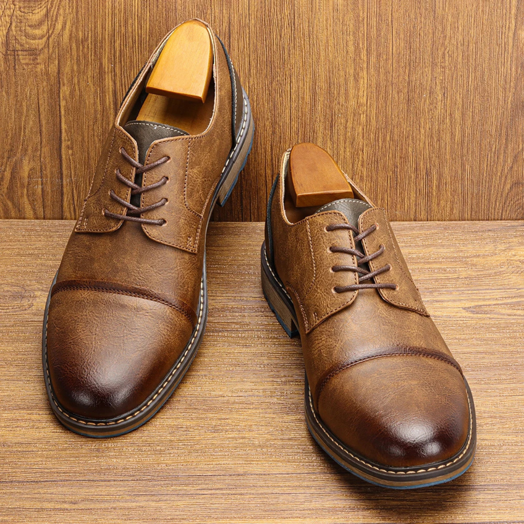 Pair of brown leather lace-up oxford shoes with blue rubber soles on wood