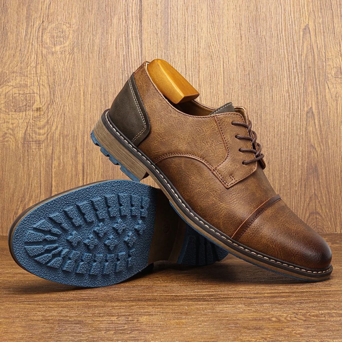 Brown leather lace-up oxford shoe with blue tread sole and gray side panel on wood