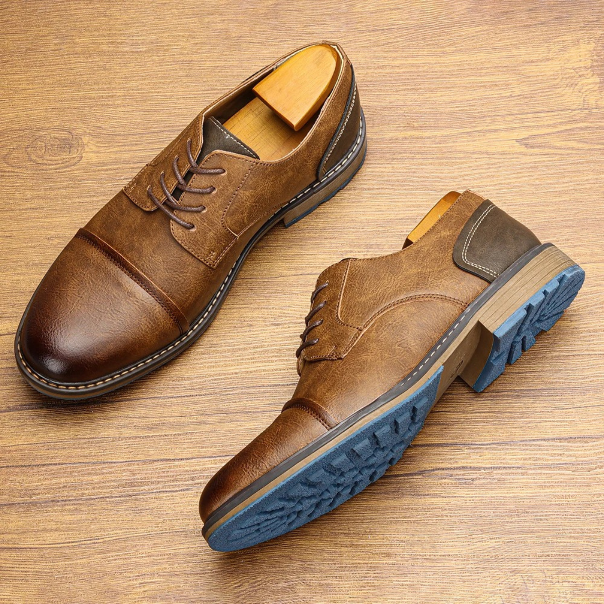 Brown leather lace-up oxford shoes laid on wood, blue tread outsoles visible