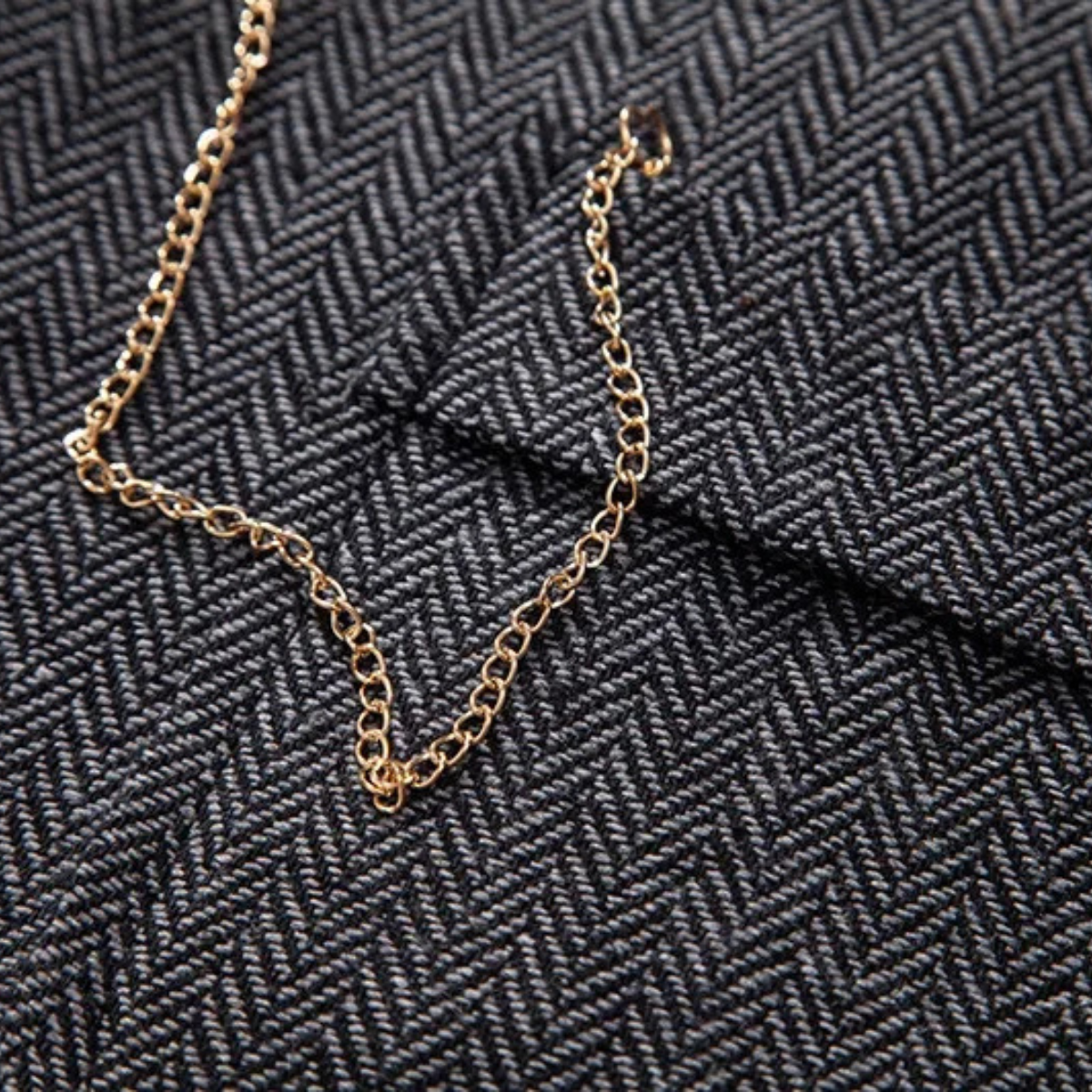 Gold chain accessory detail on dark gray tweed vest fabric