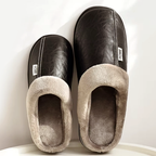 Pair of black faux leather slip-on slippers with thick beige plush lining