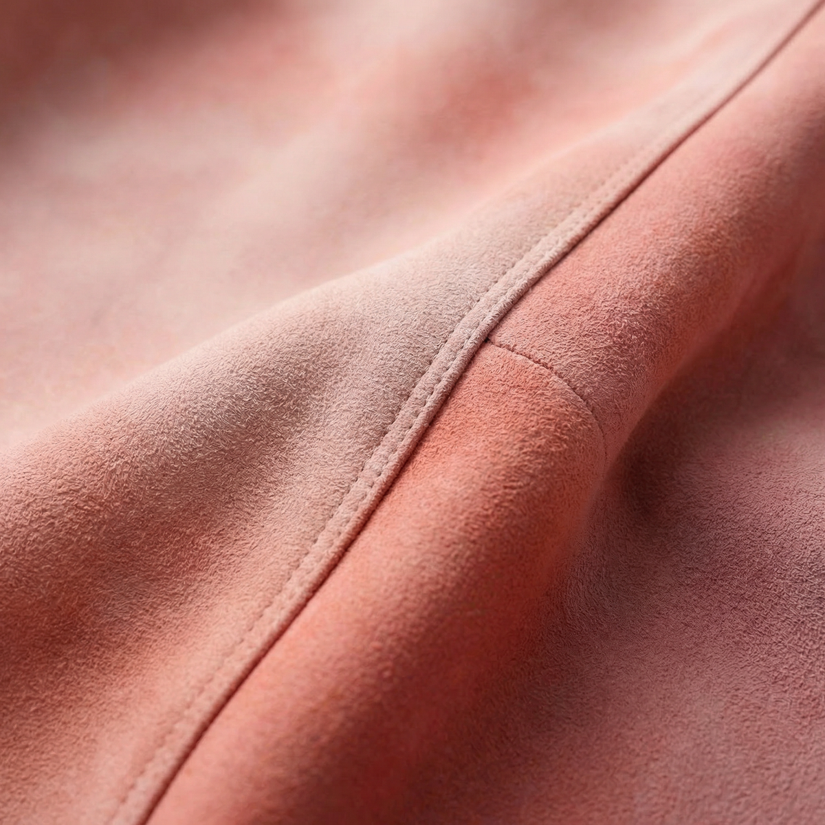 Dusty pink lambskin leather jacket fabric close-up with stitched seam and soft suede texture.