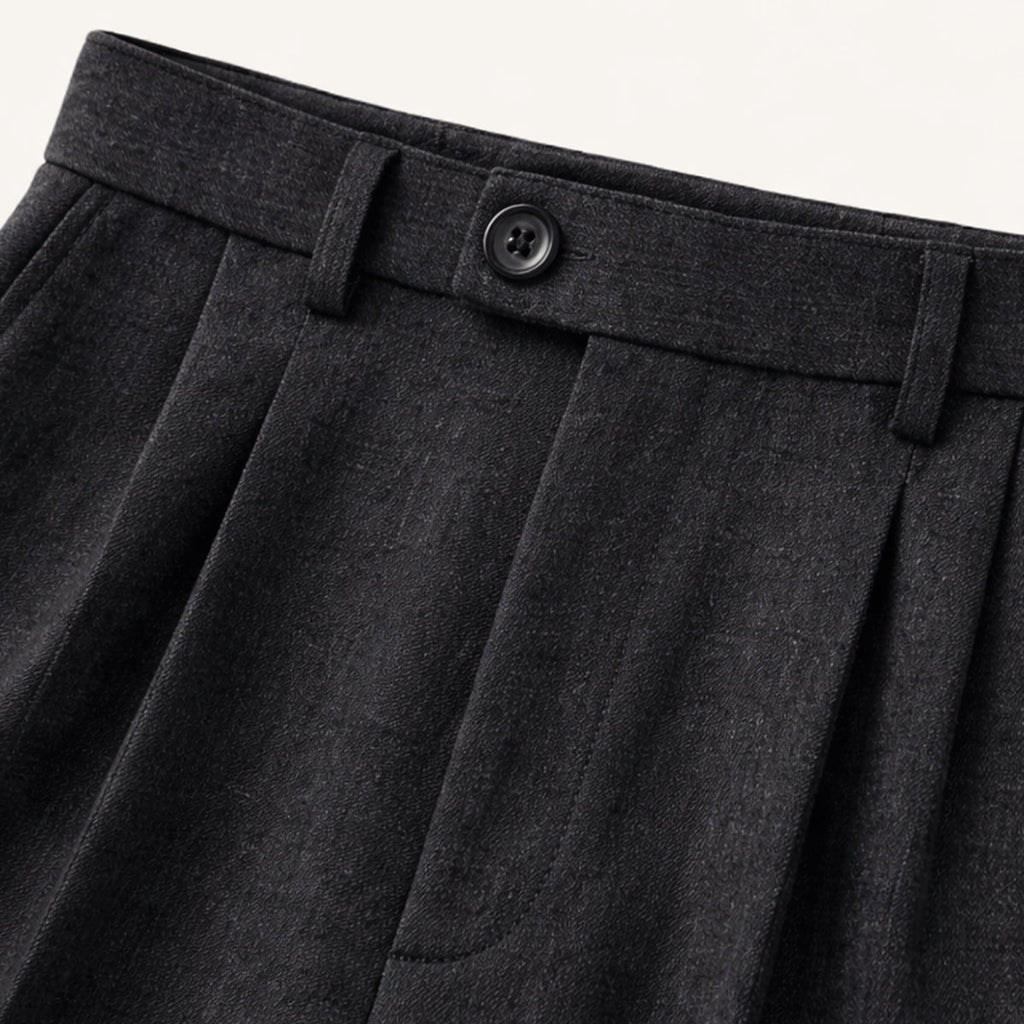 Black pleated trousers waistband with button and belt loop detail.