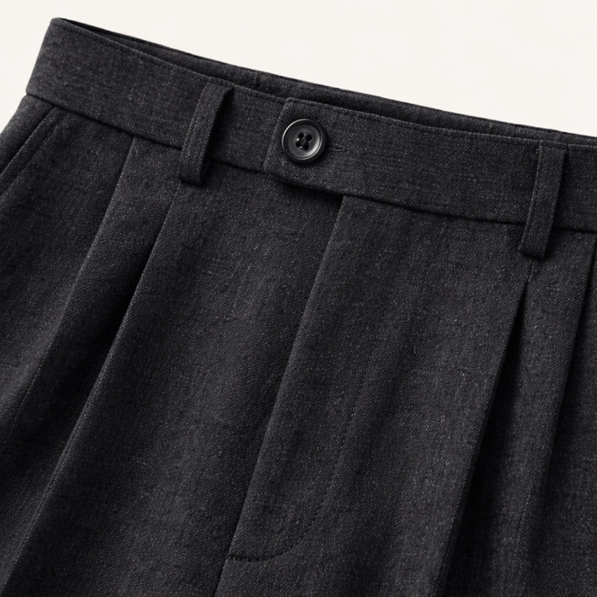 Black pleated trousers waistband with button and belt loop detail.