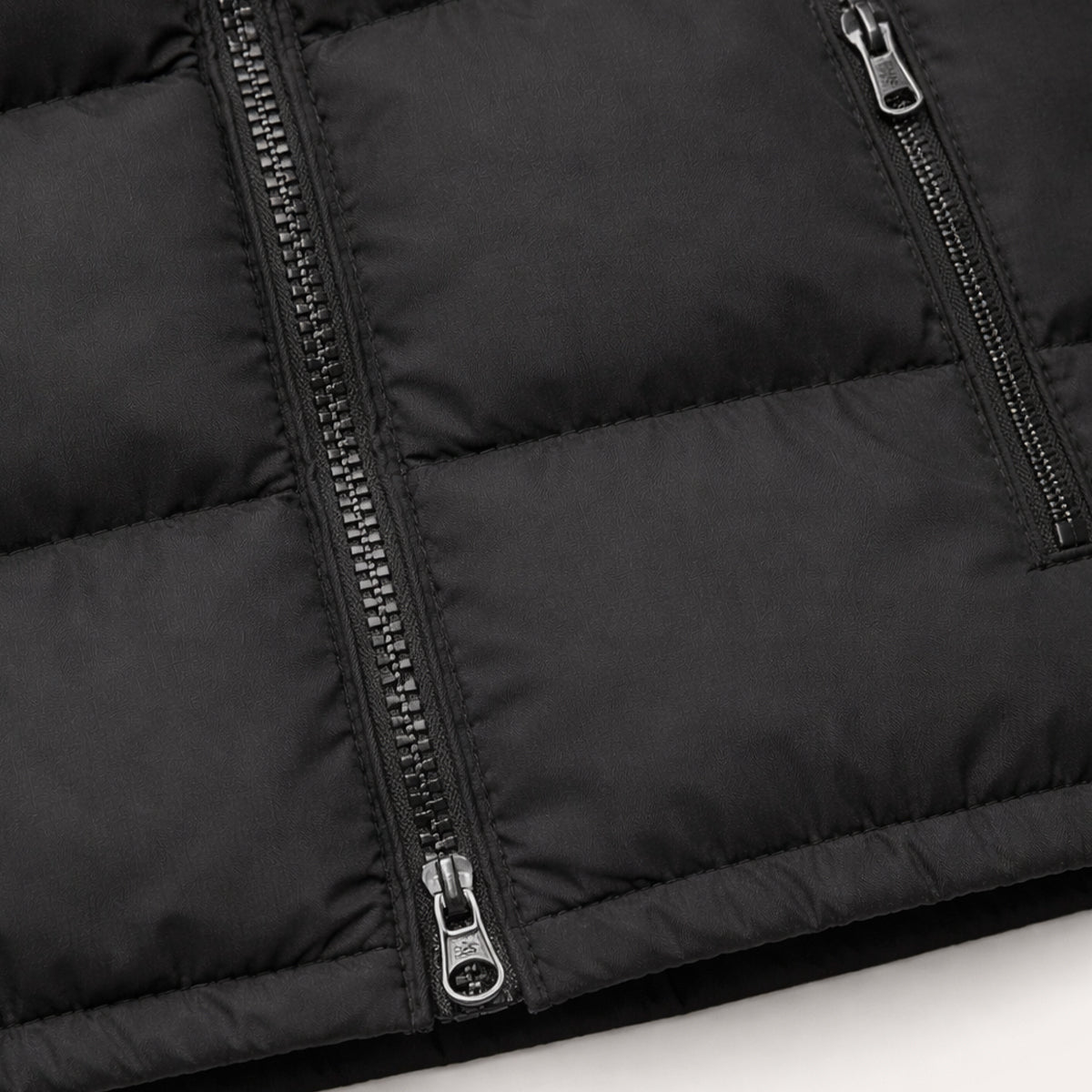 Black padded puffer vest close-up of full-zip pull and seam quilting