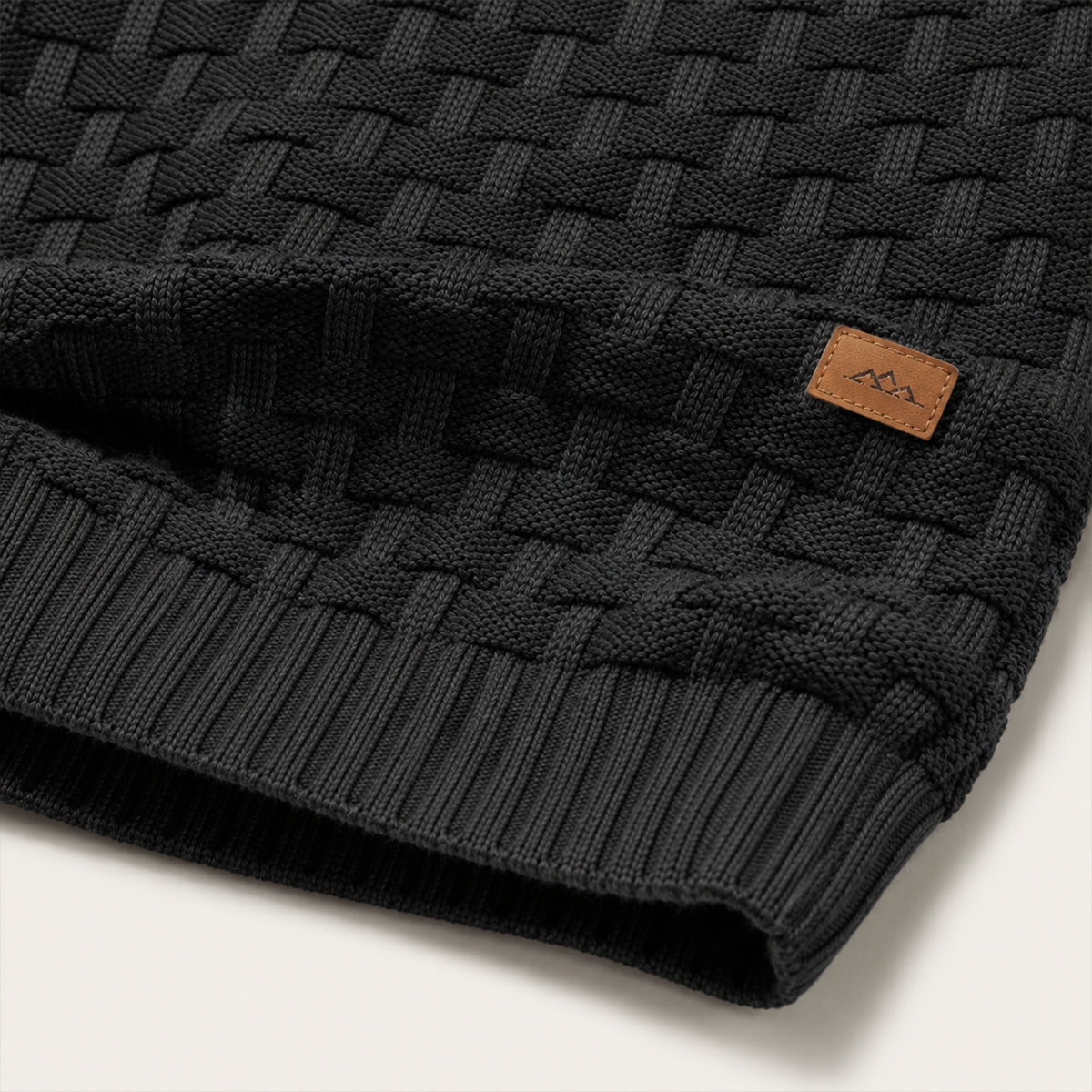 Bottom hem of dark textured knit sweater with small leather brand patch
