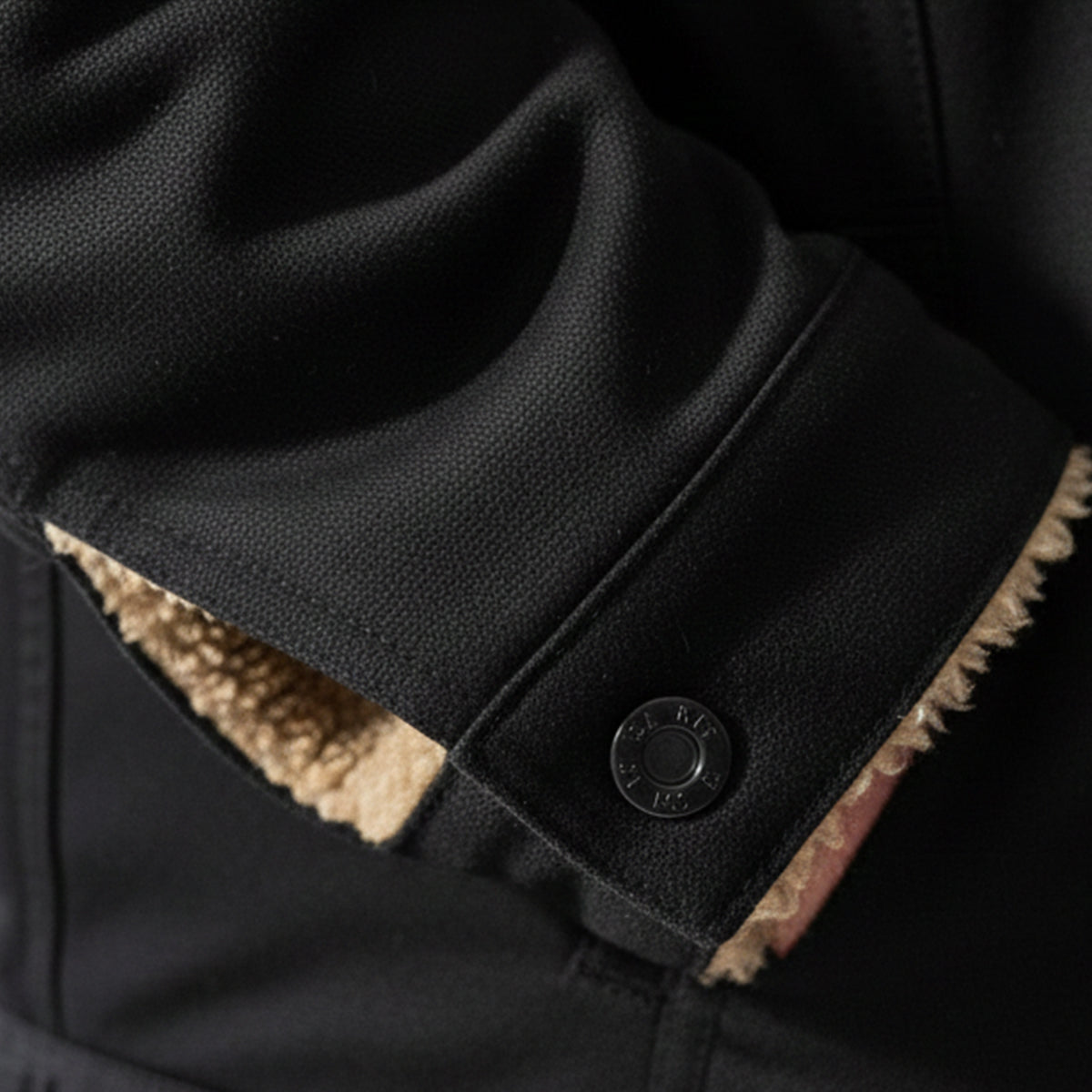 Close-up of dark navy coat cuff with tan fleece trim and round snap button
